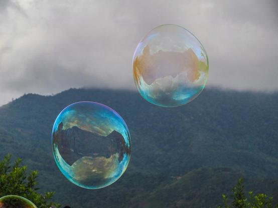 Seifenblasen steigen in den Himmel, im Hintergrund ein bewaldeter Hügelzug unter einer grauen Wolkendecke
